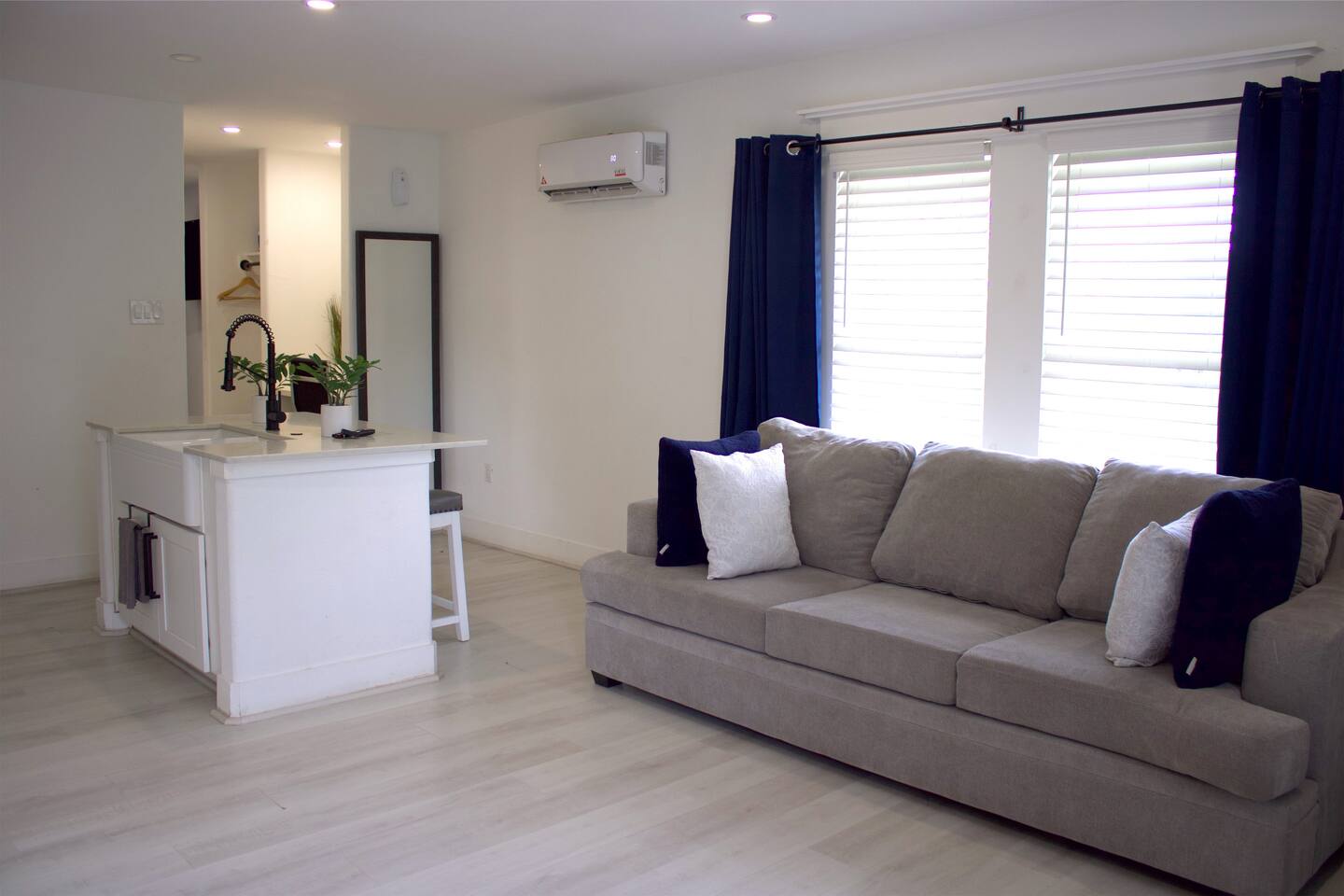 Unit 1 living room with a gray sofa, navy curtains, and a kitchen island